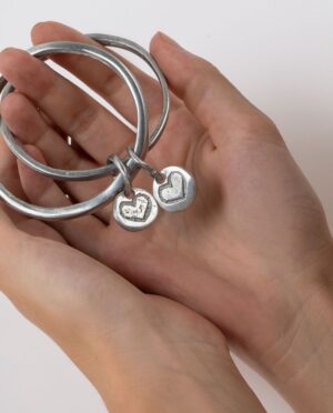 2 bracciali rigidi uniti da ciondoli cuore. Realizzato a mano in alluminio 100% riciclato.